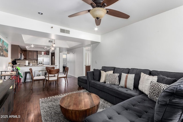 living room featuring ceiling fan, a tray ceiling, dark hardwood / wood-style flooring, and sink