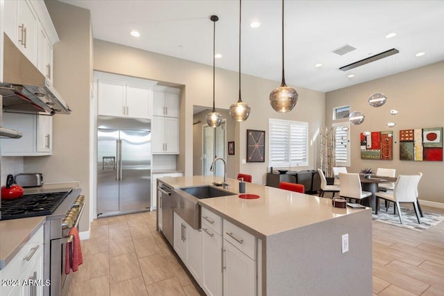 kitchen featuring white cabinets, an island with sink, pendant lighting, high end appliances, and sink