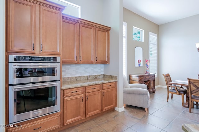 32731 N 74th Way, Scottsdale, AZ 85266 - kitchen featuring double oven, light stone counters, backsplash, baseboards, and brown cabinetry