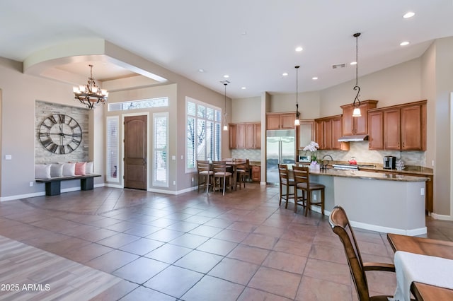 32731 N 74th Way, Scottsdale, AZ 85266 - kitchen with under cabinet range hood, stainless steel built in refrigerator, tasteful backsplash, brown cabinets, and a center island with sink