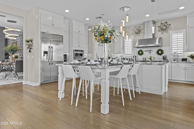 kitchen with stainless steel appliances, a kitchen island with sink, white cabinets, and decorative light fixtures