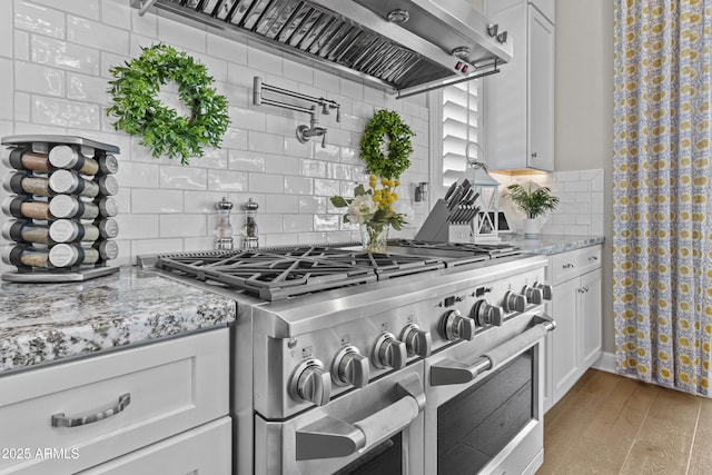 kitchen featuring range with two ovens, white cabinetry, light stone countertops, and wall chimney range hood