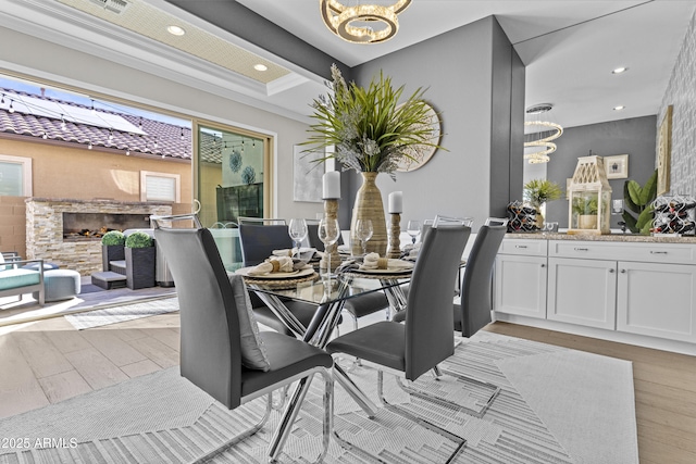 dining space with an inviting chandelier, a fireplace, light hardwood / wood-style floors, and beamed ceiling