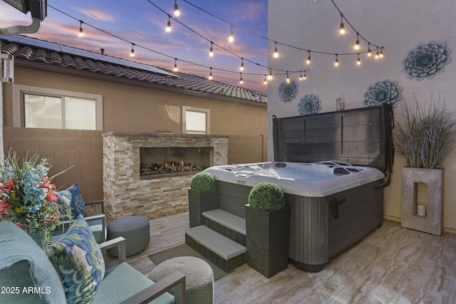 patio terrace at dusk with a hot tub and an outdoor stone fireplace