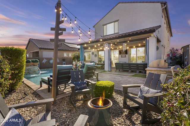 back house at dusk with pool water feature, exterior kitchen, and a patio