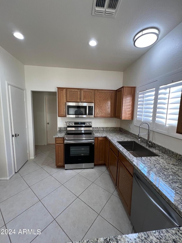 kitchen with light stone counters, light tile patterned flooring, appliances with stainless steel finishes, and sink