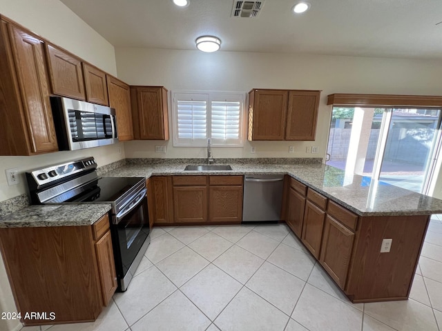 kitchen with appliances with stainless steel finishes, sink, kitchen peninsula, light stone counters, and light tile patterned floors