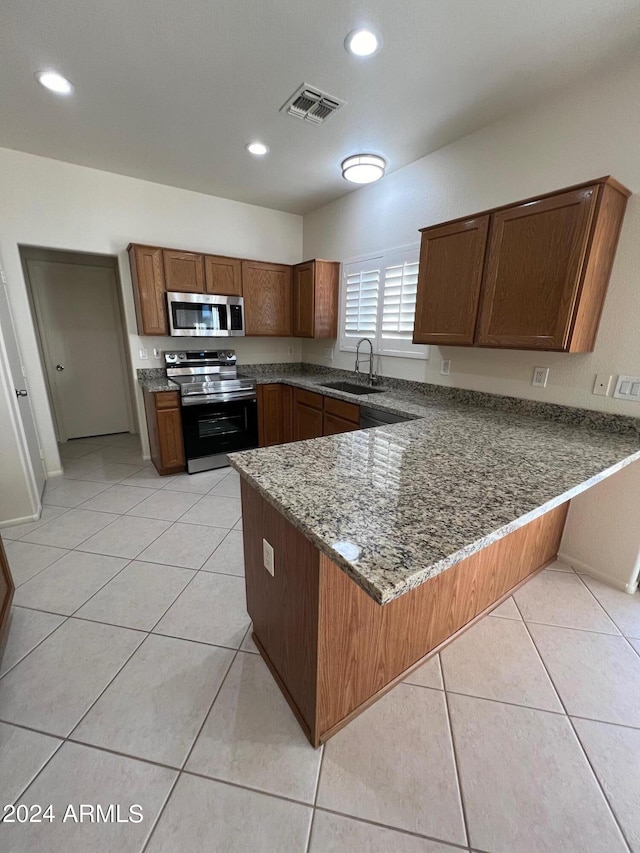 kitchen with kitchen peninsula, light tile patterned floors, dark stone counters, sink, and stainless steel appliances