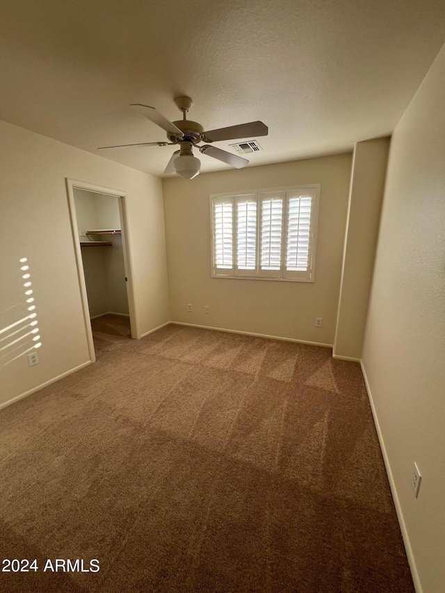 unfurnished bedroom featuring a closet, ceiling fan, carpet flooring, and a walk in closet