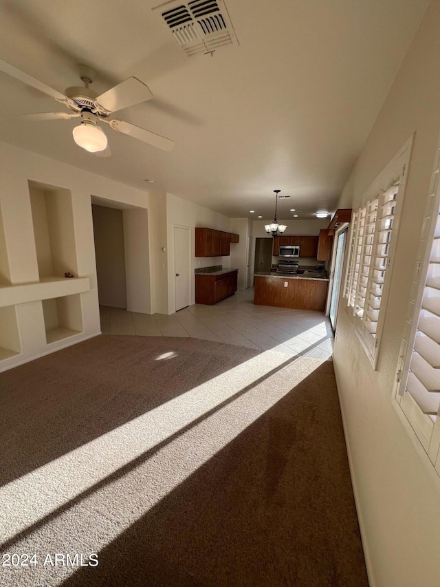 unfurnished living room with light carpet, built in shelves, and ceiling fan with notable chandelier