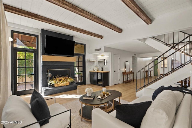 living room with a large fireplace, beamed ceiling, and light hardwood / wood-style flooring