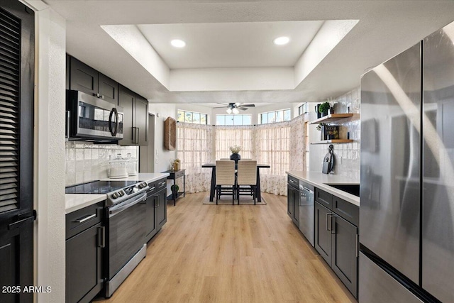 kitchen featuring ceiling fan, light wood-type flooring, backsplash, stainless steel appliances, and a tray ceiling