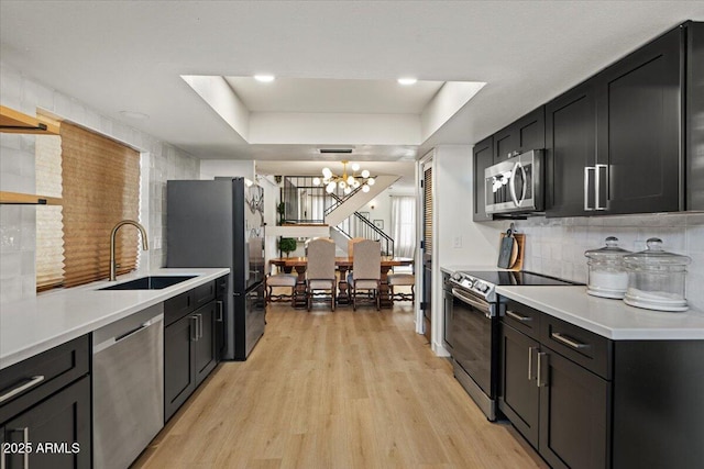 kitchen with appliances with stainless steel finishes, light hardwood / wood-style floors, sink, a raised ceiling, and a notable chandelier