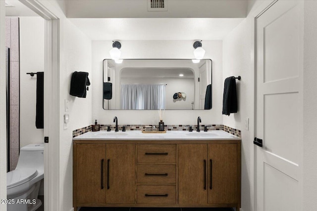 bathroom featuring toilet, vanity, and tasteful backsplash