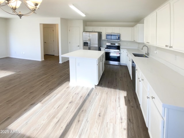 kitchen featuring an inviting chandelier, stainless steel appliances, a kitchen island, white cabinets, and sink