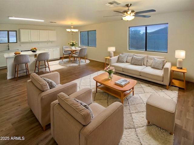 living room featuring ceiling fan with notable chandelier, sink, and light hardwood / wood-style flooring