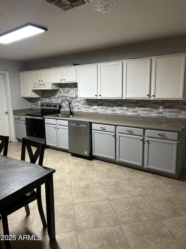 kitchen with stainless steel appliances, decorative backsplash, light tile patterned flooring, a sink, and under cabinet range hood