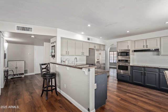 kitchen with arched walkways, gray cabinets, visible vents, appliances with stainless steel finishes, and a kitchen bar