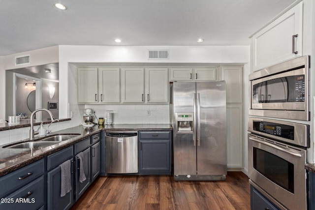 kitchen with appliances with stainless steel finishes, visible vents, a sink, and dark stone countertops