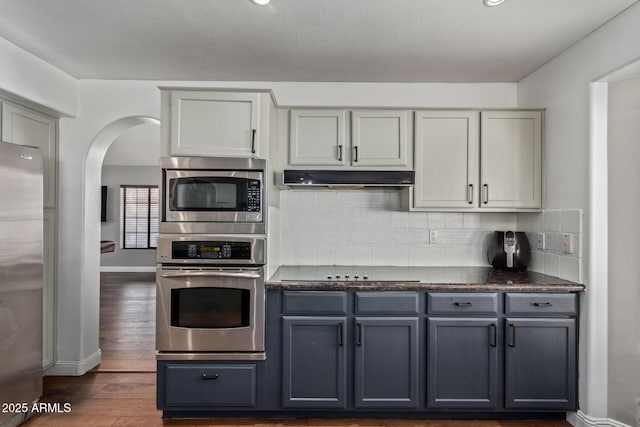 kitchen with under cabinet range hood, appliances with stainless steel finishes, backsplash, gray cabinets, and dark countertops