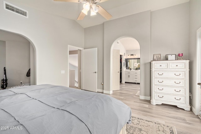 bedroom featuring arched walkways, ensuite bathroom, visible vents, baseboards, and light wood finished floors