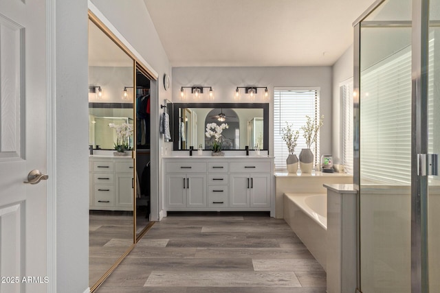 full bathroom featuring a stall shower, wood finished floors, a garden tub, and double vanity