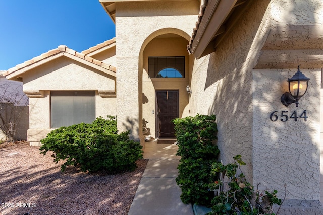 view of exterior entry featuring a tiled roof and stucco siding