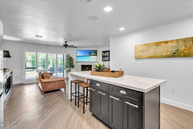 3505 N Miller Rd, Scottsdale, AZ 85251 - kitchen with crown molding, a fireplace, open floor plan, light wood-style floors, and a breakfast bar