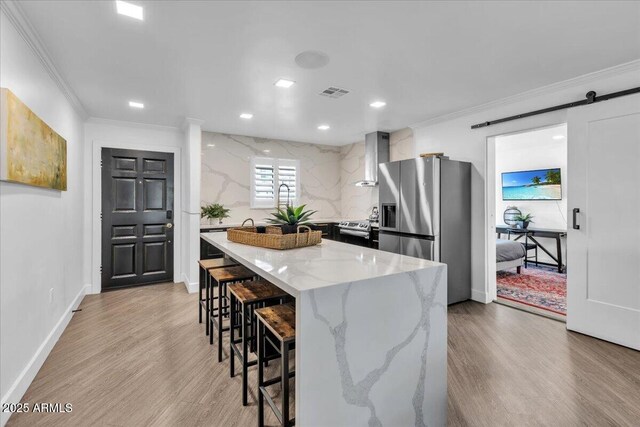 3505 N Miller Rd, Scottsdale, AZ 85251 - kitchen featuring appliances with stainless steel finishes, crown molding, wall chimney exhaust hood, a breakfast bar area, and light wood-style floors