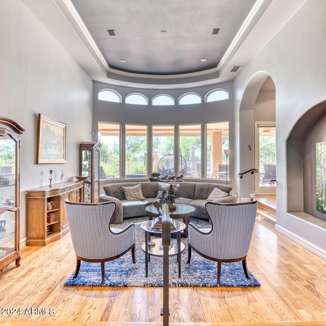 living room featuring light wood-type flooring, a tray ceiling, and a high ceiling