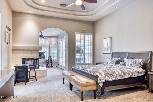 7101 E Berneil Ln, Paradise Valley, AZ 85253 - carpeted bedroom with arched walkways, a tiled fireplace, a tray ceiling, recessed lighting, and a ceiling fan