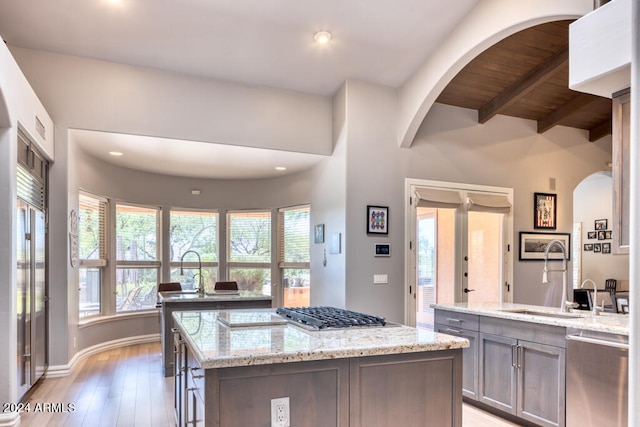 kitchen with sink, an island with sink, light hardwood / wood-style flooring, stainless steel appliances, and light stone countertops