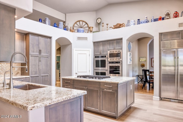 kitchen with light stone counters, a center island, and built in appliances