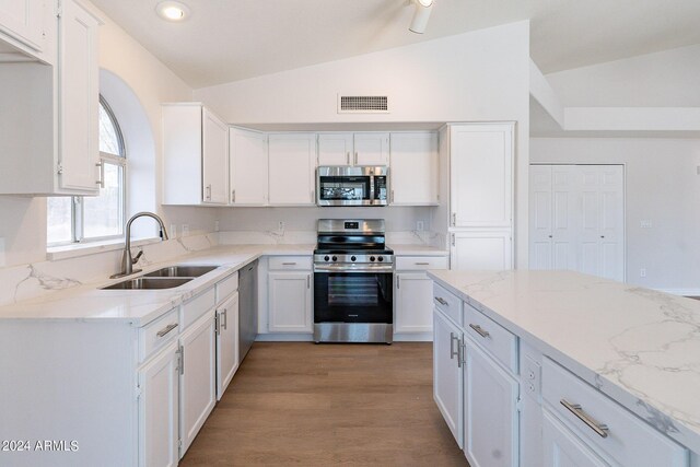 kitchen with appliances with stainless steel finishes, light hardwood / wood-style flooring, white cabinetry, sink, and vaulted ceiling