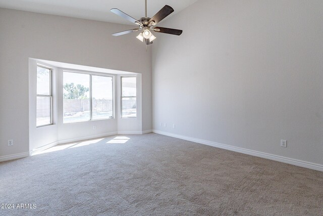 carpeted empty room with high vaulted ceiling and ceiling fan