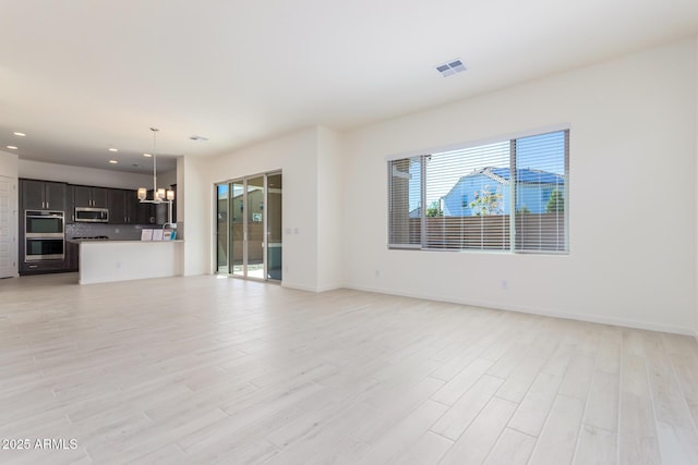 unfurnished living room with a notable chandelier and light wood-type flooring