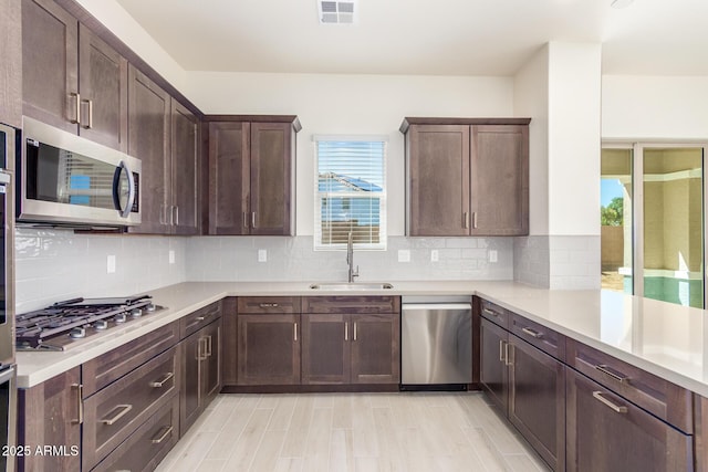 kitchen with sink, appliances with stainless steel finishes, backsplash, dark brown cabinets, and light wood-type flooring