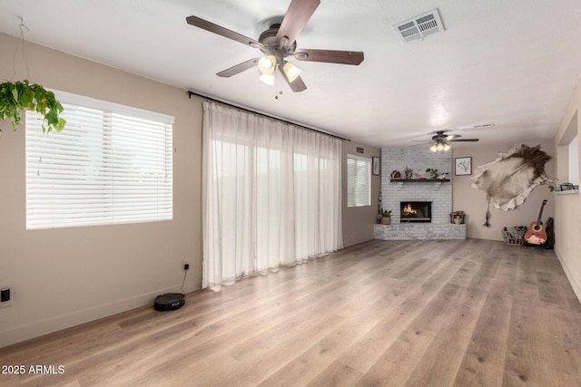 unfurnished living room featuring a ceiling fan, baseboards, visible vents, light wood-style floors, and a brick fireplace