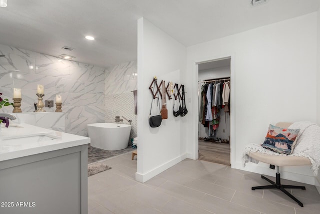 full bath with a sink, visible vents, tile walls, a soaking tub, and double vanity