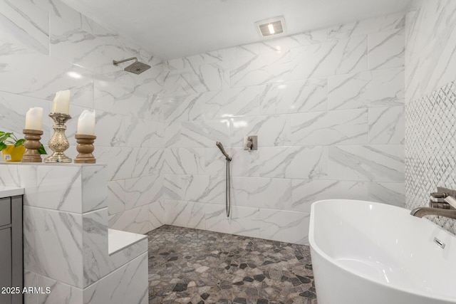 full bathroom with visible vents, a tile shower, a freestanding bath, vanity, and tile walls