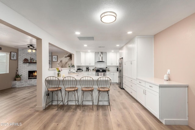 kitchen with a peninsula, visible vents, wall chimney range hood, appliances with stainless steel finishes, and a kitchen bar