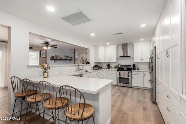 kitchen with visible vents, appliances with stainless steel finishes, a sink, wall chimney range hood, and a peninsula