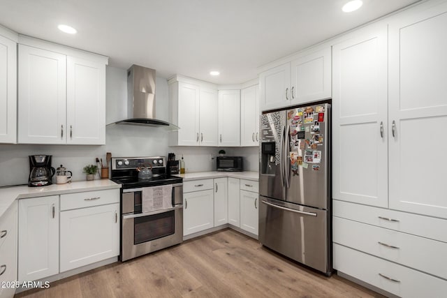 kitchen with wall chimney exhaust hood, light wood-style flooring, white cabinets, and stainless steel appliances