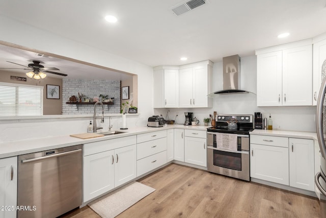 kitchen with light wood finished floors, stainless steel appliances, visible vents, white cabinets, and wall chimney range hood