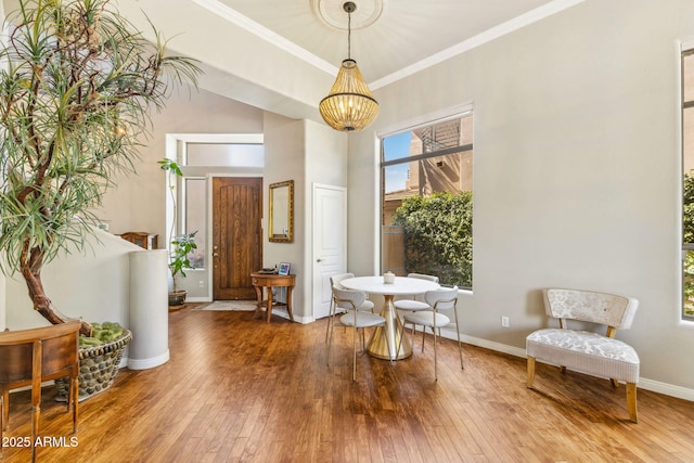 living area with baseboards, a towering ceiling, wood-type flooring, ornamental molding, and a notable chandelier