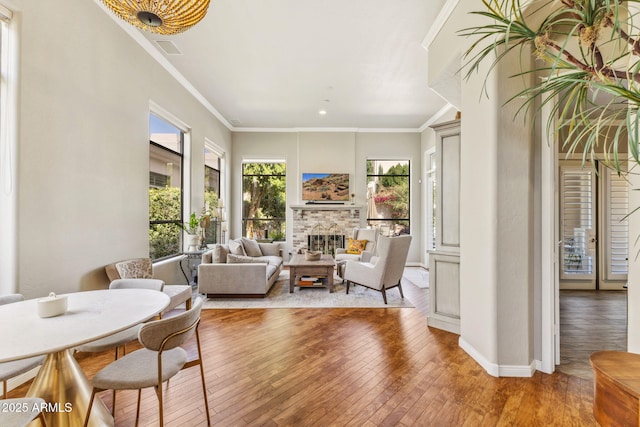 interior space with a stone fireplace, visible vents, baseboards, light wood finished floors, and crown molding