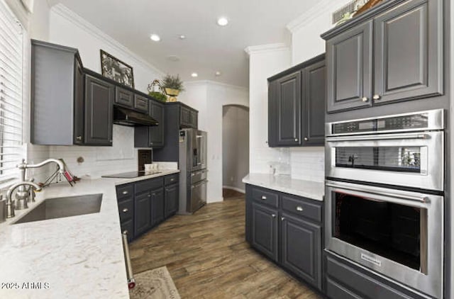 kitchen featuring arched walkways, under cabinet range hood, stainless steel appliances, a sink, and ornamental molding