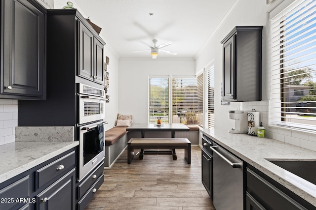 kitchen with appliances with stainless steel finishes, light wood-type flooring, dark cabinetry, and crown molding