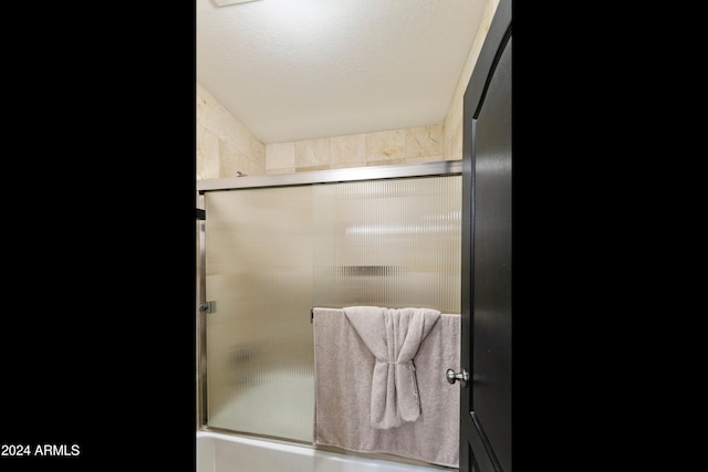 bathroom featuring combined bath / shower with glass door and a textured ceiling