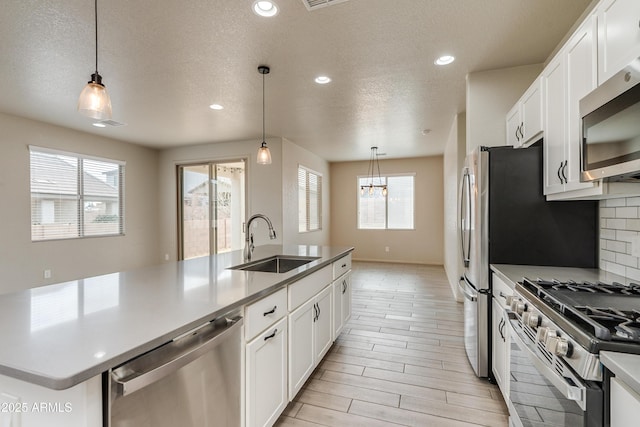 kitchen with stainless steel appliances, hanging light fixtures, sink, and a center island with sink